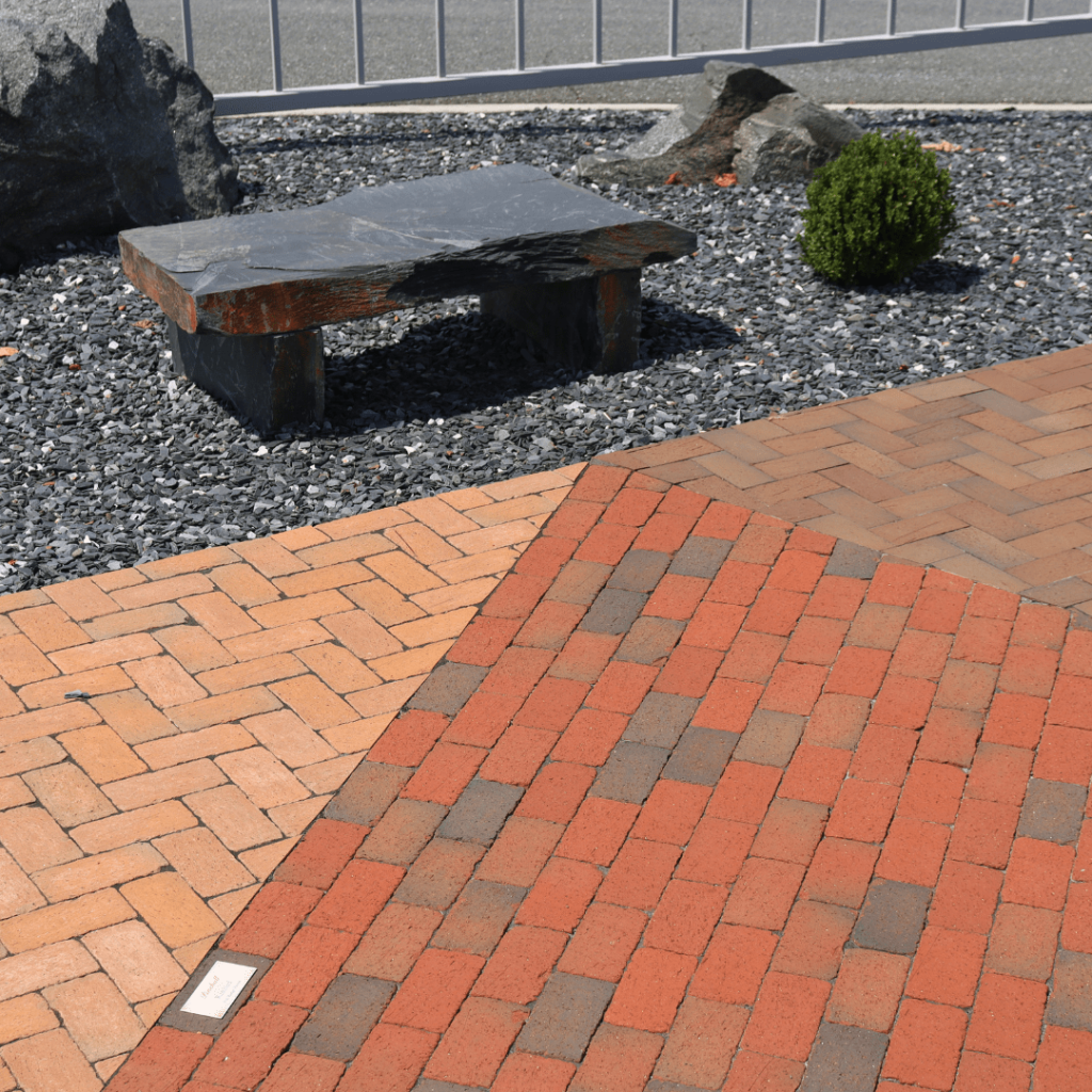 Stone bench on a patio of red clay and gray pavers in the outdoor showroom
